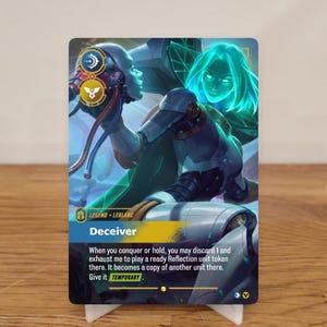 Könnte beinhalten: Eine Sammelkarte mit einer futuristischen weiblichen Figur mit blauen und grünen Akzenten. Die Karte trägt den Titel "Deceiver" und enthält Spieltext. Die Karte wird auf einem weißen Ständer präsentiert.