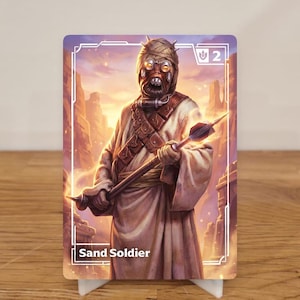 Könnte beinhalten: Eine Karte mit einer Illustration eines Sand-Soldaten. Die Figur ist in einem beigen Gewand und einer Kopfbedeckung dargestellt und hält einen Speer. Der Hintergrund zeigt eine Wüstenlandschaft bei Sonnenuntergang. Die Karte hat einen weißen Rand und den Text "Sand Soldier".