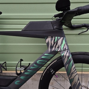 Puede incluir: Bicicleta de carretera Canyon negra y gris con un patrón de rayas de cebra único en verde y beige. La bicicleta tiene manillar negro, un portabidón y un neumático Continental Grand Prix 5000 S.
