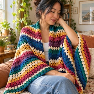 May include: A crochet shawl featuring a vibrant, multi-colored striped pattern in shades of magenta, mustard yellow, teal, and cream. The garment is crafted with a classic granny stitch design, creating a textured, open-weave fabric that drapes.