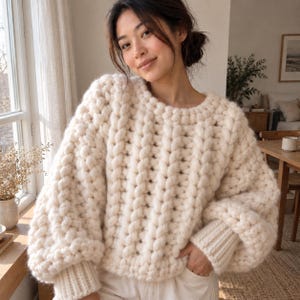 May include: A chunky, cream-colored knit sweater featuring a prominent vertical cable stitch pattern, a round neckline, and long, voluminous sleeves with ribbed cuffs. The garment is crafted from thick, heavy yarn with a textured, braided appearance.