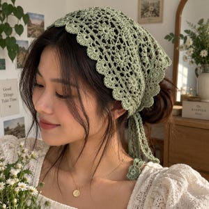 Puede incluir: Un pañuelo de ganchillo en color verde salvia con un intrincado patrón floral y un borde festoneado. Este cubrecabezas triangular está elaborado con un delicado punto calado e incluye largos lazos de ganchillo a juego en la parte posterior.