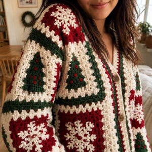 Op de afbeelding: Een gehaakt vest met lange mouwen en een patchworkontwerp van crèmekleurige, donkergroene en dieprode vierkanten. Het patroon bevat afwisselende motieven van witte sneeuwvlokken en donkergroene kerstbomen met rode accenten, afgewerkt met bruine knopen.