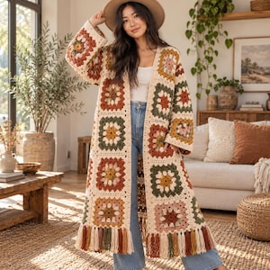 Puede incluir: Un cárdigan largo de ganchillo abierto por delante con un patrón de cuadrados de la abuela multicolor en tonos crema, naranja óxido, verde oliva y amarillo mostaza. La prenda tiene mangas anchas y flecos largos en el bajo.