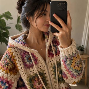 Puede incluir: Una sudadera con capucha y cremallera confeccionada con cuadrados de ganchillo multicolores. La prenda presenta una base de color crema con patrones florales en tonos rosa, amarillo, azul y verde, con capucha y cordones a juego.