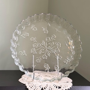 May include: A white ceramic mug with a black handle and the text "But First, Coffee" in a bold, black font. The mug is filled with a dark liquid, probably coffee, and rests on a light-coloured surface.