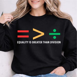 May include: Black sweatshirt with the message "EQUALITY IS GREATER THAN DIVISION" in white. The graphic includes a red equal sign, a yellow greater than symbol, and a green division symbol.