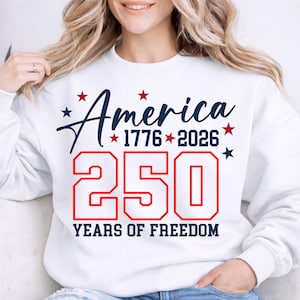 May include: White sweatshirt with the text "America 1776-2026 250 Years of Freedom" in navy blue and red. The design includes stars. A casual, patriotic apparel item.