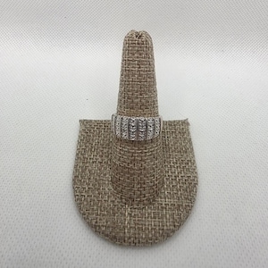 May include: A silver ring with multiple rows of small, clear gemstones. The ring is displayed on a brown ring holder against a white background. The ring's design features a series of parallel bands, each set with the gemstones.