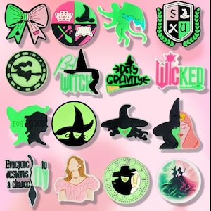 May include: A collection of green, pink, and black charms featuring various designs. The charms include a bow, witch hats, text that says "Wicked", and silhouettes of witches. The charms are likely for shoes or accessories.