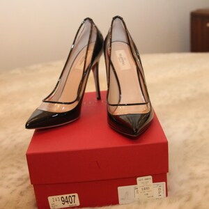 Puede incluir: Un par de zapatos de tac&oacute;n negros de charol con paneles de PVC transparentes. Los zapatos se exhiben en una caja roja. Los tacones son de estilo stiletto. Los zapatos tienen puntas puntiagudas y un dise&ntilde;o delicado.