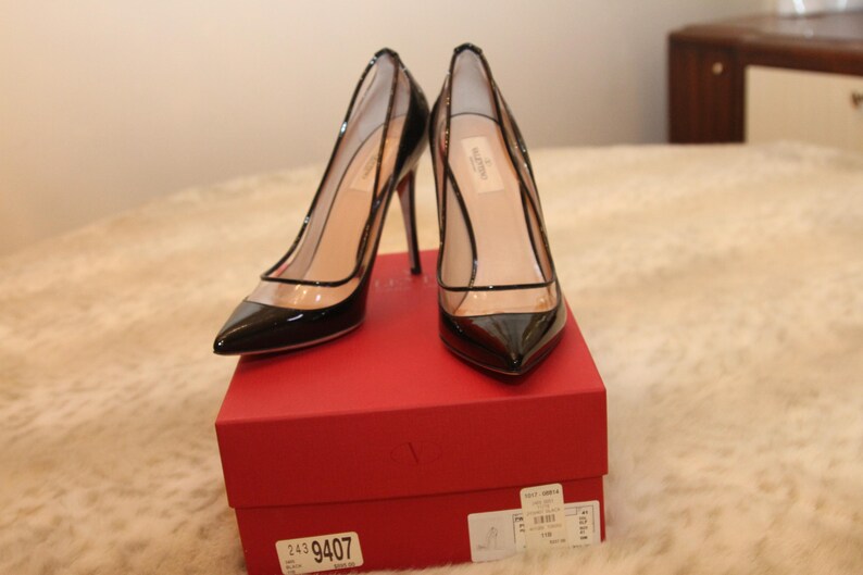 Puede incluir: Un par de zapatos de tac&oacute;n negros de charol con paneles de PVC transparentes. Los zapatos se exhiben en una caja roja. Los tacones son de estilo stiletto. Los zapatos tienen puntas puntiagudas y un dise&ntilde;o delicado.