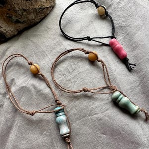 May include: Three handmade decorative bottle stoppers. One is black with a pink stopper, one is brown with a light blue stopper, and one is brown with a green stopper. Each stopper has a small tassel.