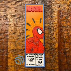 Puede incluir: Un gráfico rectangular con temática de Marvel con Spider-Man. El diseño incluye el logotipo de Marvel en naranja, una ilustración de Spider-Man rojo y negro, y texto que indica el precio y la aprobación de la Comics Code Authority.