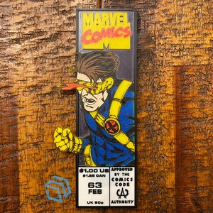 May include: A rectangular enamel pin featuring Cyclops from X-Men in a blue and yellow suit with a red visor. The top displays the Marvel Comics logo, while the bottom includes text reading $1.00 US, $1.25 CAN, 63 FEB, UK 60p, and Comics Code Authority.