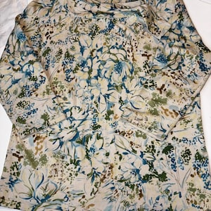 Puede incluir: Una camisa de manga larga con un estampado floral en tonos beige, azul, verde y marrón. La camisa presenta un cuello redondo y un corte holgado. El diseño floral se extiende por toda la prenda.