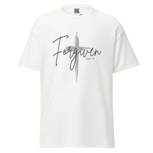 Puede incluir: Camiseta blanca con un diseño de cruz gris y la palabra "Forgiven" en fuente cursiva. El texto "1 John 1:9" está debajo de la palabra "Forgiven". La camiseta está hecha de un material suave.