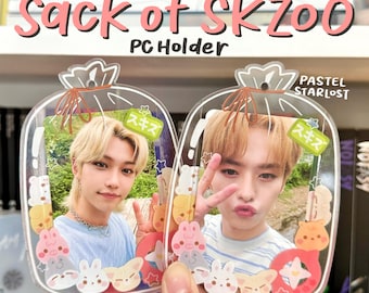 May include: Clear acrylic PC holder with a "Sack of SKZoo" design. Each holder features a photo of a person, surrounded by cartoon animal illustrations. The text "PC Holder" and "PASTEL STARLOST" are visible.