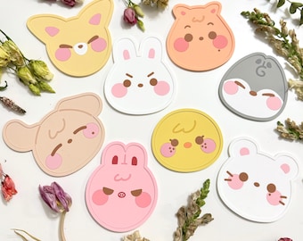 Könnte beinhalten: Eine Sammlung von neun bunten Untersetzern in Form von Cartoon-Tieren. Die Untersetzer zeigen Designs von Hund, Kaninchen, Hamster, Bär, Küken und Maus in Gelb, Orange, Rosa, Weiß und Grau. Jeder Untersetzer hat rosa Rouge-Details.