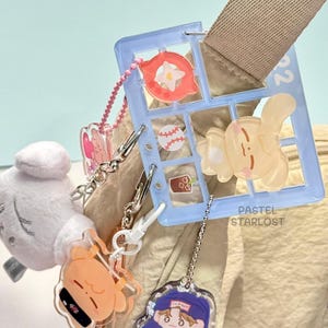 May include: A selection of pastel keychains and charms. A light blue window-shaped charm features cartoon images, alongside a plush white bear and other character charms. The text "PASTEL STARLOST" is visible.