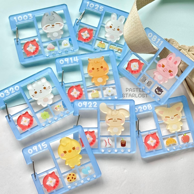 May include: A selection of light blue acrylic charms featuring cartoon animal characters, such as a rabbit, bear, and fox. Each charm is set within a window-shaped frame and numbered. The text "PASTEL STARLOST" is visible.