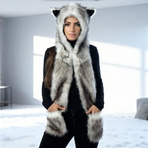 Può includere: Un cappuccio e sciarpa in finta pelliccia grigia, bianca e nera. Il cappuccio presenta orecchie a punta e la sciarpa si estende sul davanti con tasche. Il capo è progettato per assomigliare a un lupo o una volpe.