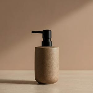 Könnte beinhalten: Ein gesprenkelter, brauner Keramik-Seifenspender mit schwarzer Pumpe. Der Spender hat einen abgerundeten Boden und einen zylindrischen Körper. Die Pumpe ist oben positioniert und einsatzbereit. Der Hintergrund ist einfarbig und neutral.