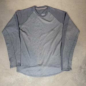 Op de afbeelding: Een shirt met lange raglanmouwen in twee grijstinten. De romp is lichtgrijs gemêleerd, terwijl de mouwen en de kraag donkergrijs zijn. Op de rechterbovenkant van de borst staat een klein, donker logo gedrukt.
