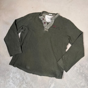 May include: An olive green long-sleeve henley shirt with a textured waffle-knit fabric. The shirt features a buttoned placket with two dark buttons, a ribbed collar, and the text Abercrombie & Fitch with the number 92 embroidered on the chest.