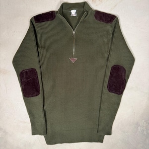 Może przedstawiać: Oliwkowozielony sweter z prążkowanej dzianiny z zapięciem na ćwierć zamka i ciemnobordowymi zamszowymi naszywkami na łokciach i ramionach. Sweter ma mały skórzany trójkątny detal u podstawy zamka. Klasyczny styl vintage.