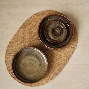 May include: A set of four round ceramic bowls with a mottled dark green and brown glaze. Three bowls are nested inside one another, while the fourth bowl is placed separately to the side. Each bowl features a smooth, glossy finish and dark rims.
