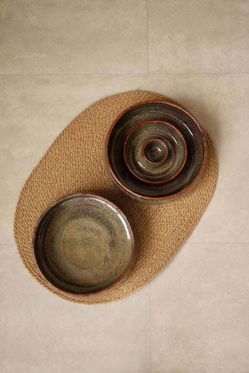 May include: A set of four round ceramic bowls with a mottled dark green and brown glaze. Three bowls are nested inside one another, while the fourth bowl is placed separately to the side. Each bowl features a smooth, glossy finish and dark rims.