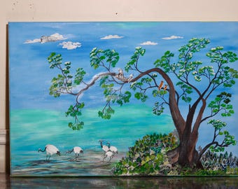 A large arching tree sheltering small birds while cranes wade through calm turquoise waters.