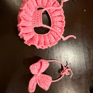 May include: A handmade, pink crocheted baby bonnet with a ruffled edge and attached ties. A matching pink crocheted bow is also included. The bonnet and bow are made of soft yarn, perfect for a newborn.