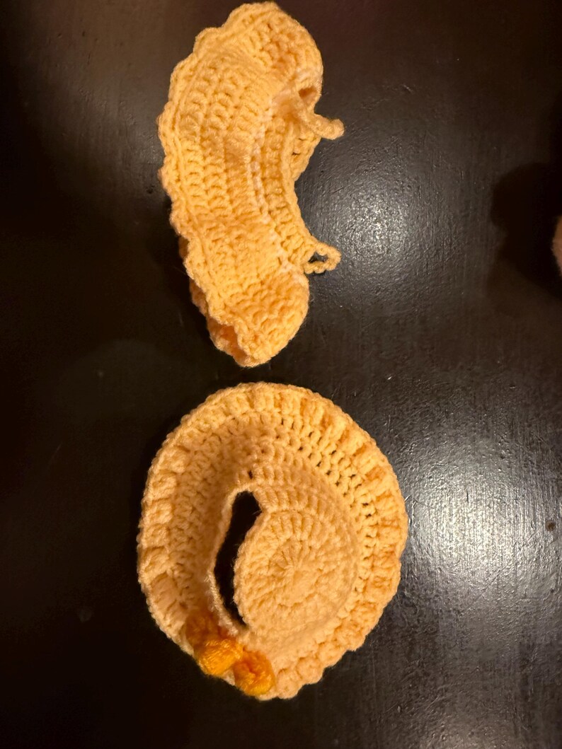 May include: Two handmade, crocheted items in a light orange color are displayed against a dark background. One item is a spiral shape, and the other is a curved shape. Both items have a textured, handmade appearance.