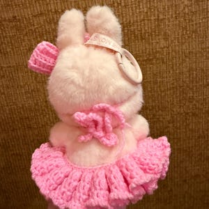May include: A plush pink bunny toy with a crocheted pink tutu and bow. The bunny has a tag that reads "THE MONST". The toy is soft and fluffy, with a cute and whimsical design.