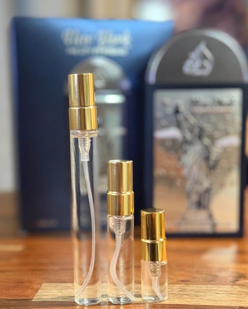 Pu&ograve; includere: Tre vaporizzatori di profumo in vetro trasparente con tappi color oro. I vaporizzatori sono di diverse dimensioni, con una scatola blu e un astuccio nero e argento sullo sfondo. I vaporizzatori sono su una superficie di legno.