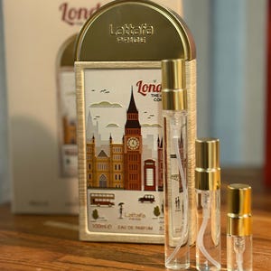 Pu&ograve; includere: Un set di profumi con tre flaconi spray trasparenti con tappi dorati, insieme a una scatola decorativa. La scatola mostra un'illustrazione a tema Londra con il Big Ben e un autobus rosso. Il marchio "Lattafa Pride" &egrave; visibile.