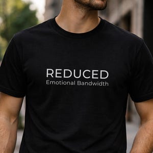 Puede incluir: Camiseta negra de cuello redondo con el texto blanco "REDUCED Emotional Bandwidth". La camiseta está hecha de un material suave y es adecuada para ropa casual. La camiseta es de estilo clásico.