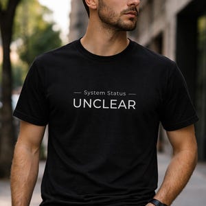 以下が含まれることがあります： 白文字で「System Status - UNCLEAR」と書かれた黒のクルーネックTシャツ。柔らかい素材でできており、カジュアルウェアに適しています。シンプルでモダンなデザインで、普段使いに最適です。