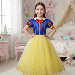 Può includere: Una bambina indossa un costume ispirato a Biancaneve. L'abito presenta un corpetto blu con dettagli rossi e una gonna gialla. Le maniche sono corte e a sbuffo, con dettagli rossi e gialli. Un fiocco rosso adorna lo scollo.