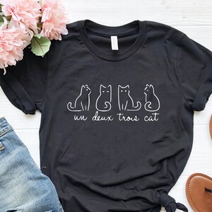 May include: Black t-shirt with a white graphic of four cats and the text "un deux trois cat".