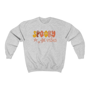 May include: A gray sweatshirt with the text "SPOOKY vibes" in orange, yellow, and pink letters. There are three pink stars above the text.