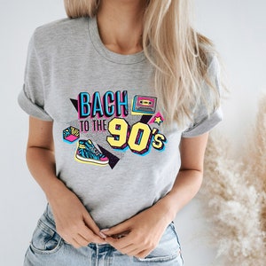 May include: Gray t-shirt with a graphic print that says "Back to the 90's" in colorful, retro-style lettering. The graphic also includes a cassette tape, a star, and a sneaker.