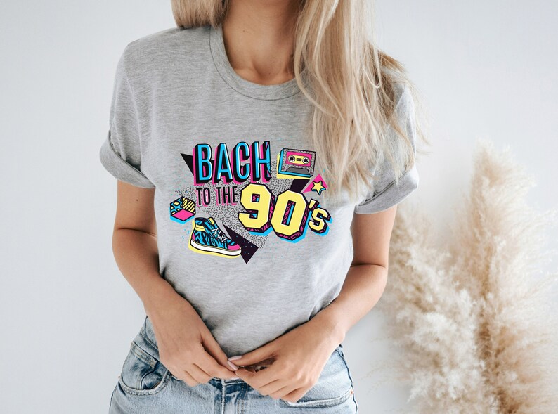 May include: Gray t-shirt with a graphic print that says "Back to the 90's" in colorful, retro-style lettering. The graphic also includes a cassette tape, a star, and a sneaker.