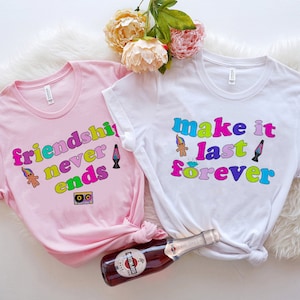 May include: Two pink and white t-shirts with a retro 80s theme. The pink shirt says "friendship never ends" with a troll doll, lava lamp, and cassette tape graphic. The white shirt says "make it last forever" with a troll doll and lava lamp graphic.