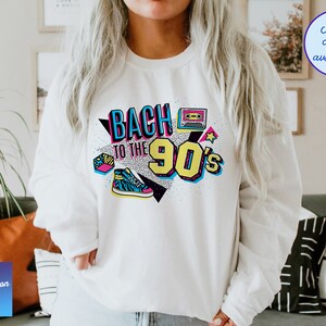 May include: White sweatshirt with a graphic print that says "Back to the 90's" in colorful, retro-style lettering. The graphic also includes a cassette tape, a star, and a sneaker.