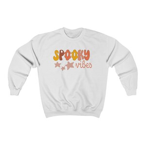 May include: White sweatshirt with the text "SPOOKY vibes" in orange, yellow, and pink letters with two pink stars.