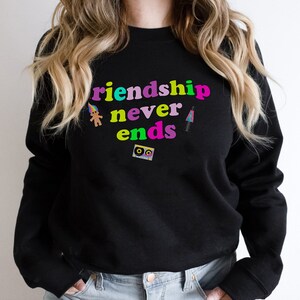 May include: Black sweatshirt with the text "Friendship never ends" in rainbow colors. The text is surrounded by small graphic images of a troll doll, a cassette tape, and a lava lamp.