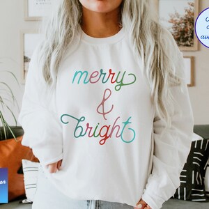 May include: White sweatshirt with the text "merry & bright" in colourful cursive lettering.